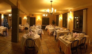 A restaurant with multiple tables set for dining, featuring a warm interior and a Christmas tree in the background. - Hotel Mirador (Lles)