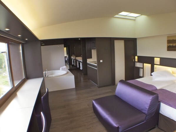Una habitación de hotel moderna con sofá, cama, una mesita y baño con bañera.