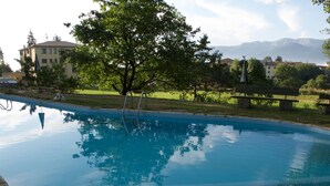 A swimming pool with a clear reflection of trees and buildings, surrounded by a grassy area and a stone border. - Hotel Mirador (Lles)