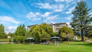 A building with a stone facade, surrounded by a grassy area with trees and outdoor seating. - Hotel Mirador (Lles)