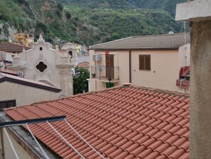 Ein Gebäude mit rotem Ziegeldach, einem Balkon mit Geländer und Blick auf eine Hügelterrasse.