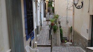 A narrow alleyway with a white chair, a potted plant, and a metal gate. - Casa Love Marina (Scilla)