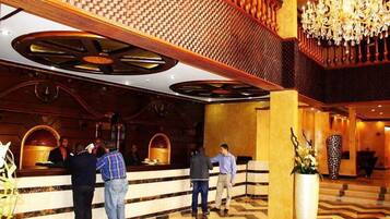 A hotel lobby with a reception desk, a chandelier, and a large potted plant.