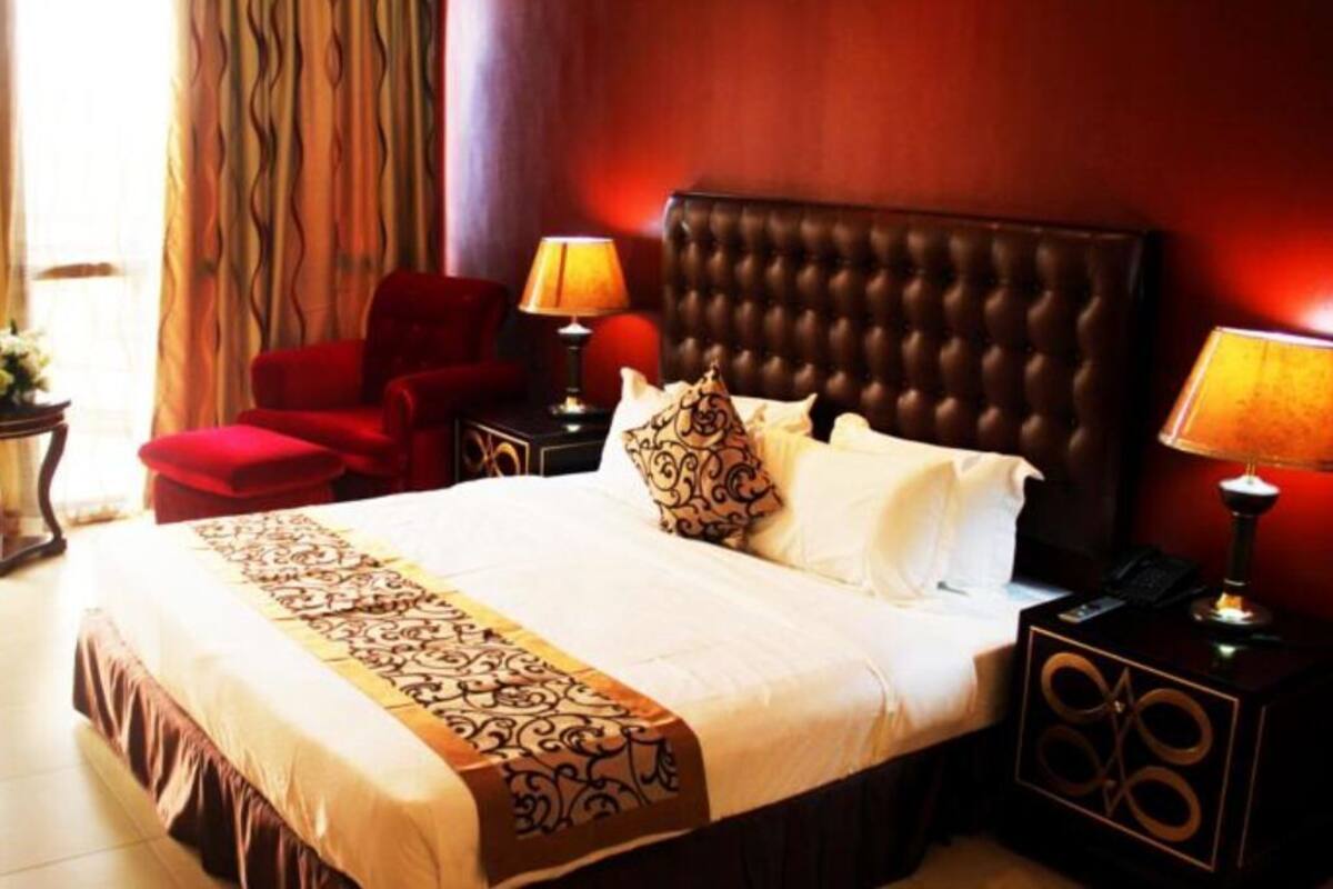 A hotel room with a large bed, two bedside tables, a red armchair, and a window with curtains.