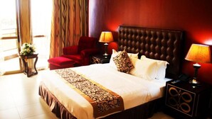 A hotel room with a large bed, two bedside tables, a red armchair, and a window with curtains. - Beatrice Hotel (Kinshasa)