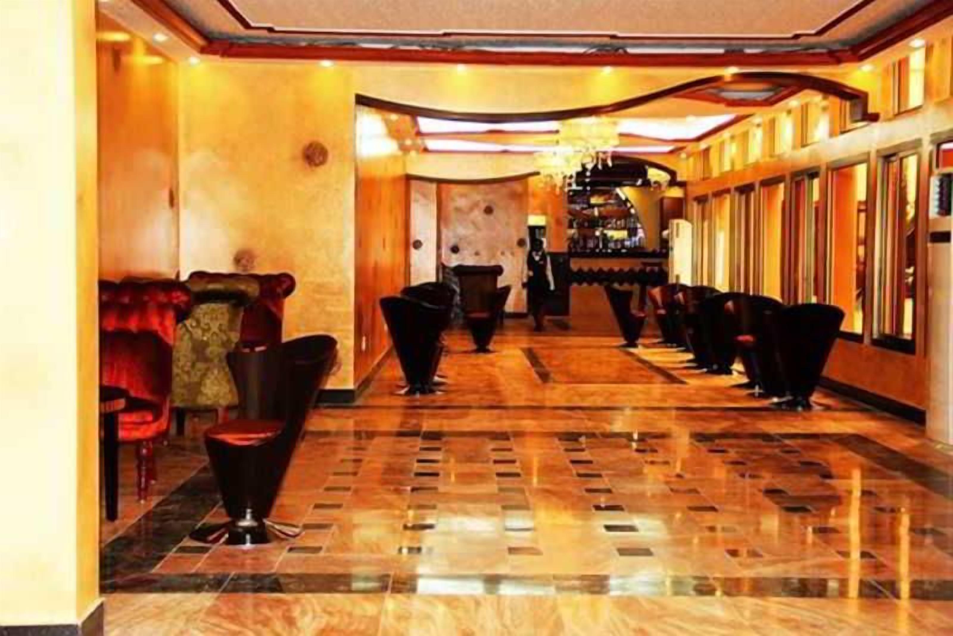 Un hall de hotel con suelo de mármol, asientos tapizados en rojo y una fila larga de sillas negras.