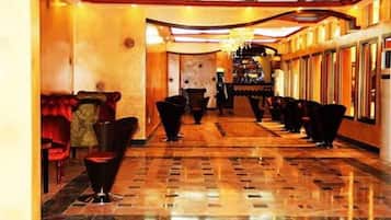 Un hall de hotel con suelo de mármol, asientos tapizados en rojo y una fila larga de sillas negras.