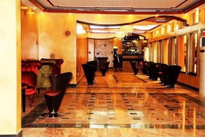 A hotel lobby with a marble floor, red upholstered seating, and a long row of black chairs. - Beatrice Hotel (Kinshasa)