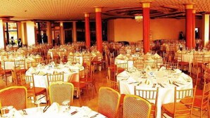 A banquet hall with round tables set for dining, red columns, and a patterned ceiling. - Beatrice Hotel (Kinshasa)