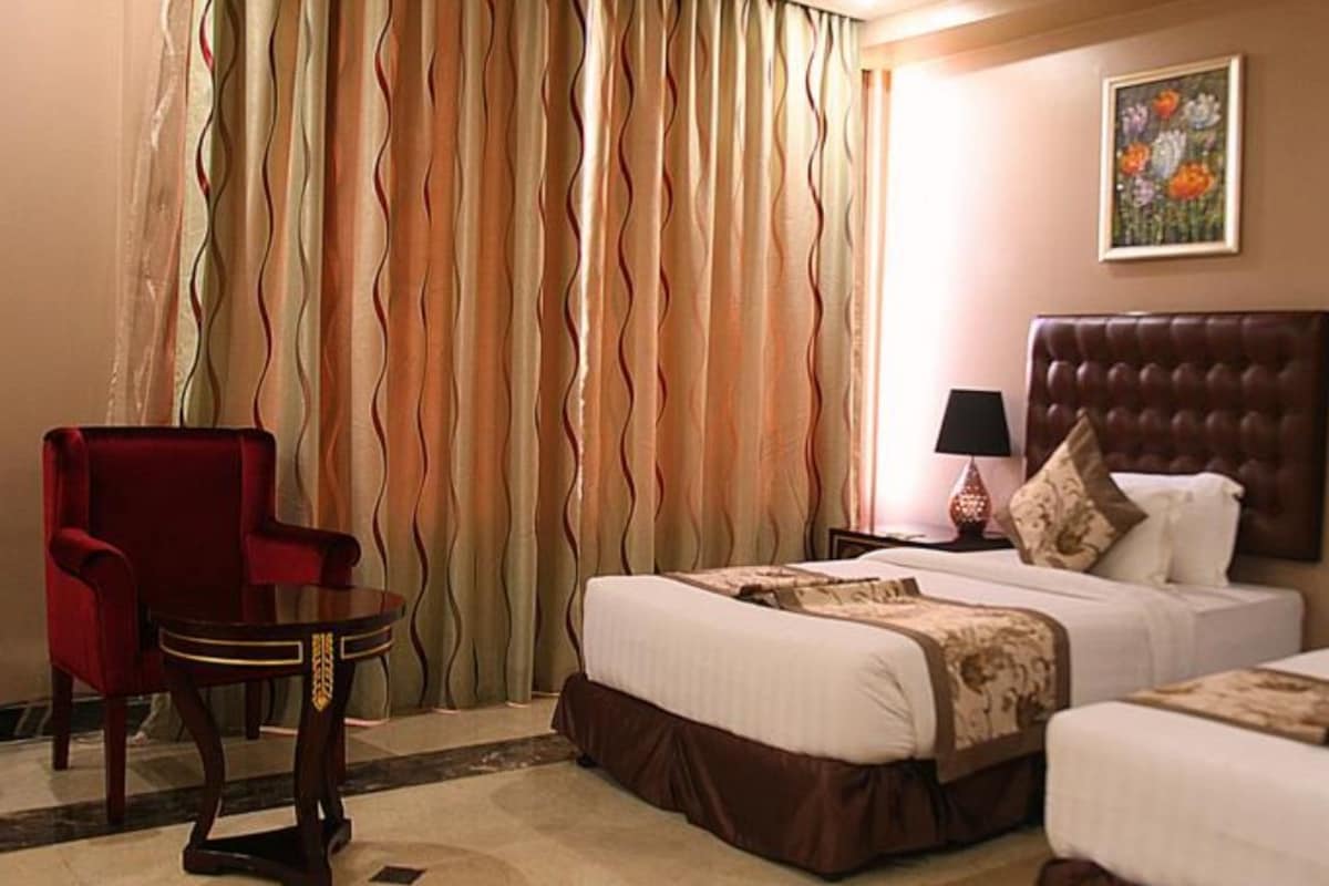 A hotel room with two beds, a red armchair, a small table, and a painting on the wall.