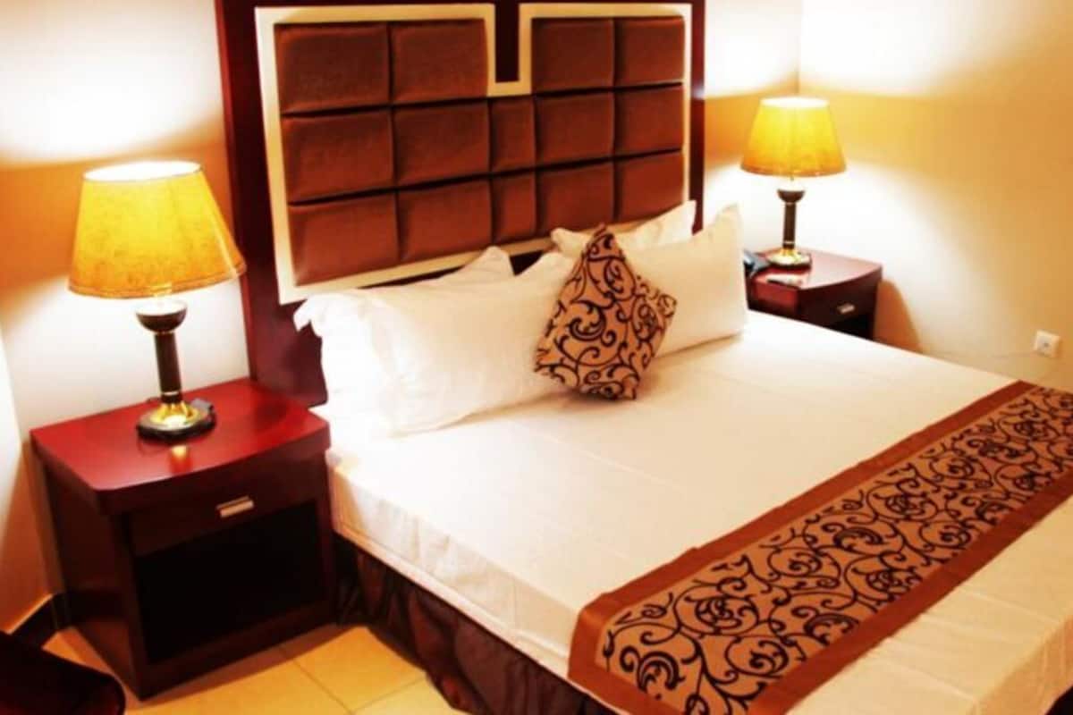 A hotel room with a large bed, two bedside lamps, a headboard, and a decorative throw blanket.