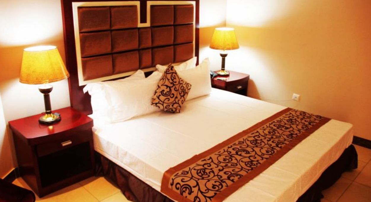 A hotel room with a large bed, two bedside lamps, a headboard, and a decorative throw blanket.