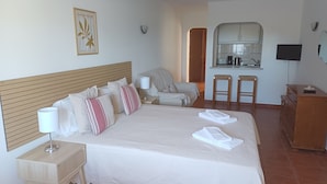 Een hotelkamer met een groot bed, nachtkastje, stoel, kleine kitchenette en televisie.