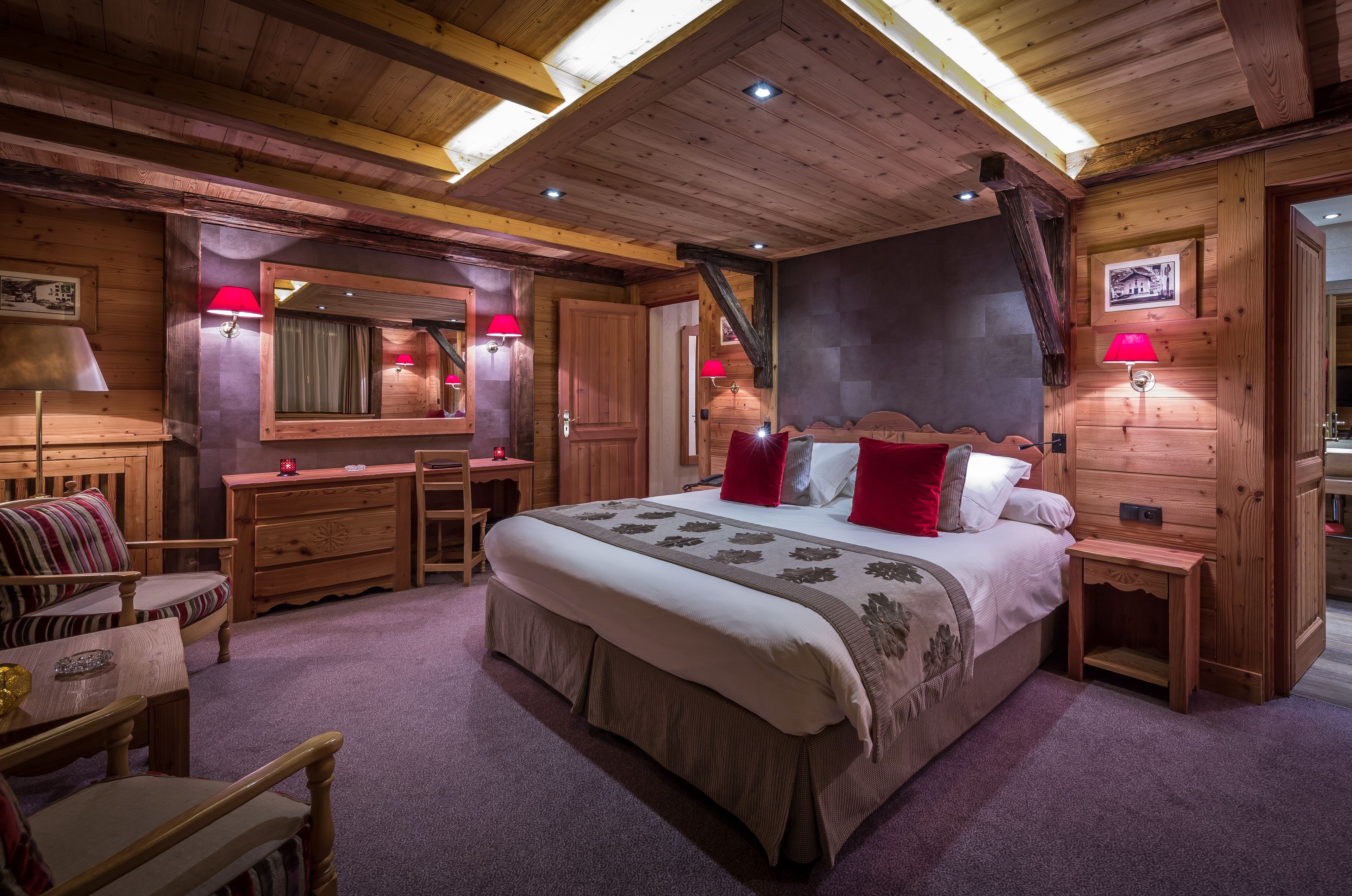 A wooden-themed bedroom with a large bed, bedside tables, a dresser, and a mirror.