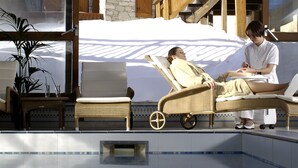 A poolside area with a lounge chair and a person sitting nearby.