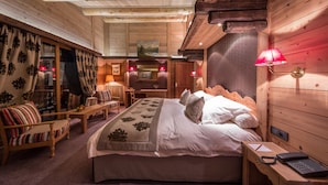 A cozy wooden cabin room with a large bed, a wooden desk, and a chair.