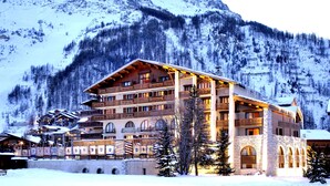A multi-story hotel with a ski lift in the background, surrounded by snow-covered mountains.