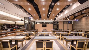 Un espace repas moderne, doté de plusieurs tables et chaises, d’un coin café et d’un téléviseur à écran plat fixé au mur.