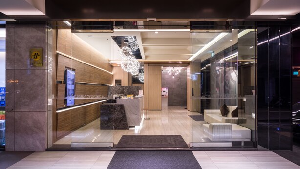 Un hall d’hôtel moderne avec un comptoir d’accueil, un espace salon et un lustre.