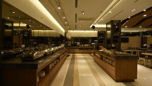 Un hall d’hôtel moderne avec un îlot central, un long comptoir servant de buffet et des murs recouverts de miroirs.