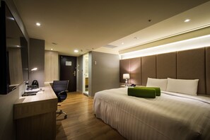 A modern hotel room with a large bed, a desk with a chair, a flat-screen TV, and a bathroom visible through an open door. - FM Hotel (Taichung)