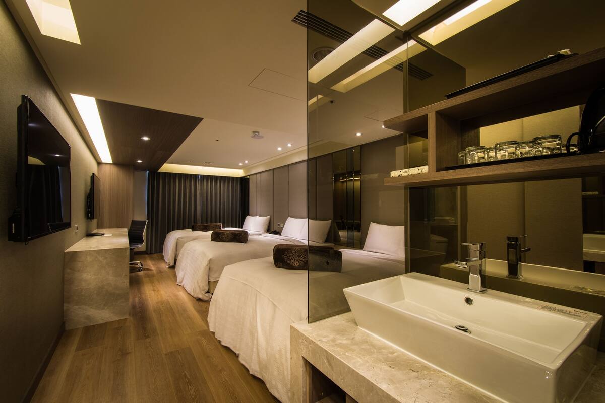A modern hotel room with a large bed, a desk, and a bathroom with a large mirror and sink.