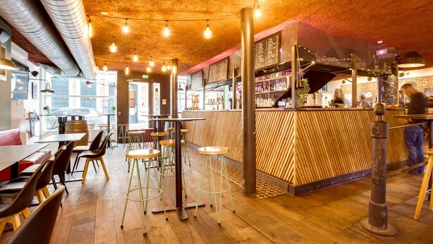 Un interior de restaurante con pisos de madera, taburetes altos y una zona de bar.