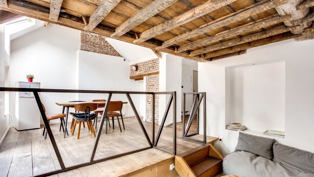 A modern interior with exposed wooden beams, a dining area with chairs and a table, and a grey sofa. - The People Lille (Lille)