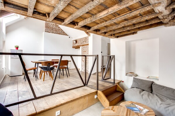 Un interior moderno con vigas de madera a la vista, un comedor con sillas y una mesa, y un sofá gris.