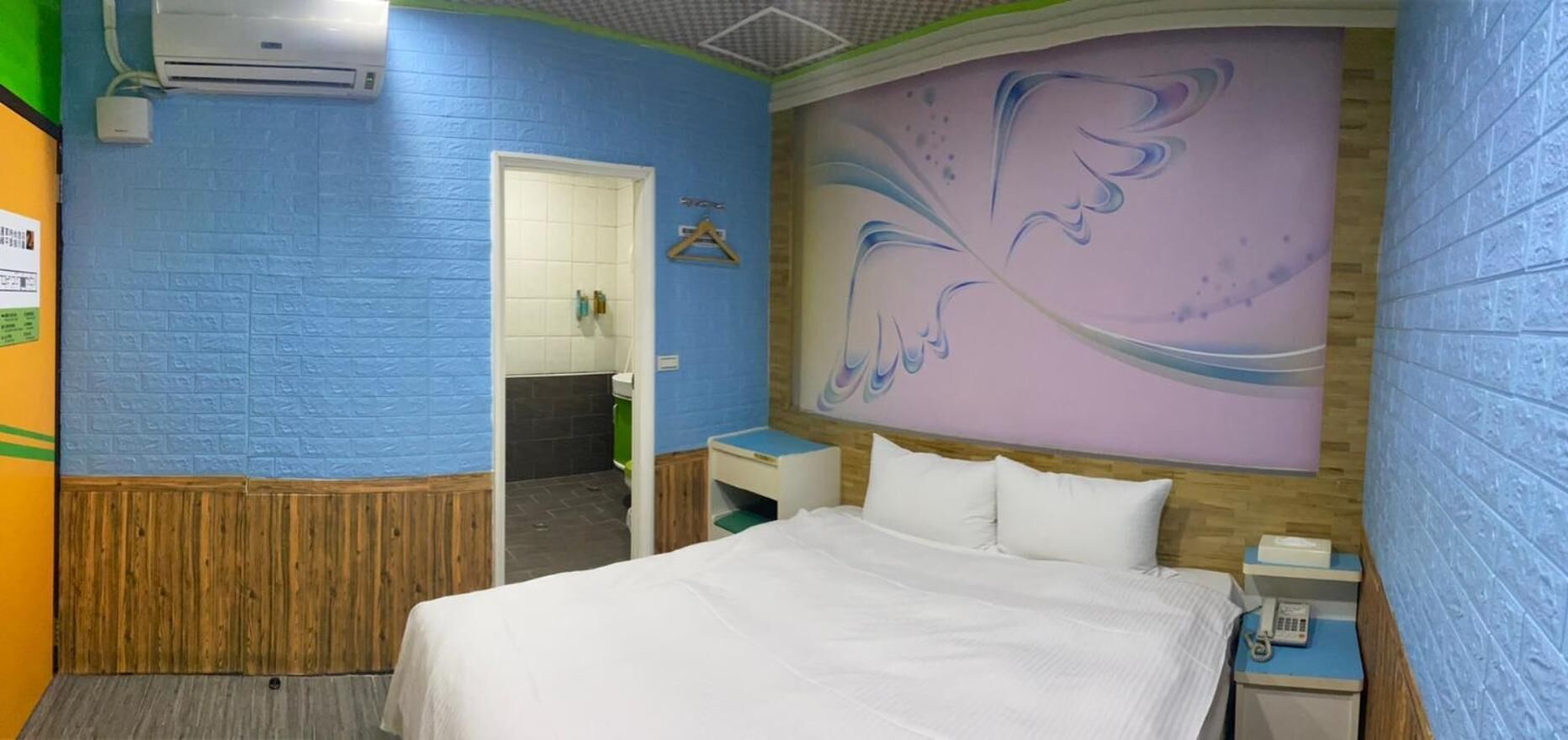 A hotel room with a bed, a nightstand, a wall-mounted telephone, and a bathroom door.