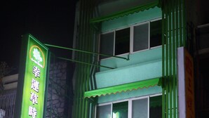Un hotel con fachada verde y señalización en inglés y chino.