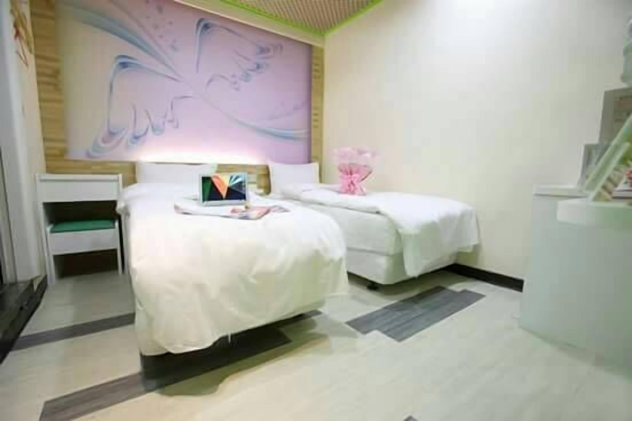 A hotel room with two beds, a large abstract painting on the wall, and a small table with a vase of flowers.