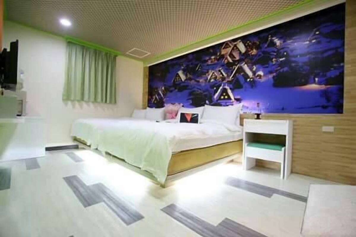 Un dormitori amb un llit, una tauleta de nit, un mural a la paret i una finestra amb cortines.