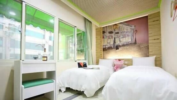 Habitación de hotel con dos camas, un escritorio y una ventana que da a un edificio.