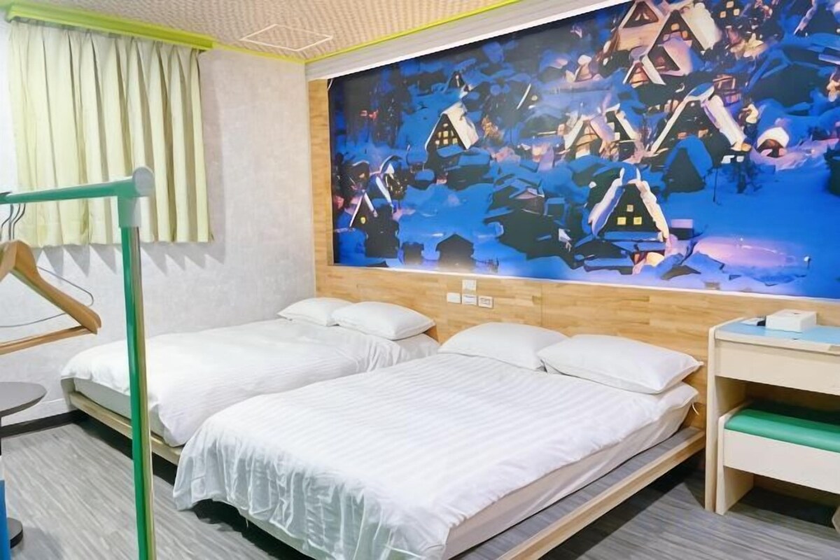 A hotel room with two beds, a wooden headboard, a wall mural, a desk, and a chair.