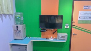 Una habitación con escritorio, televisión, dispensador de agua, refrigerador pequeño y una puerta con un cartel.
