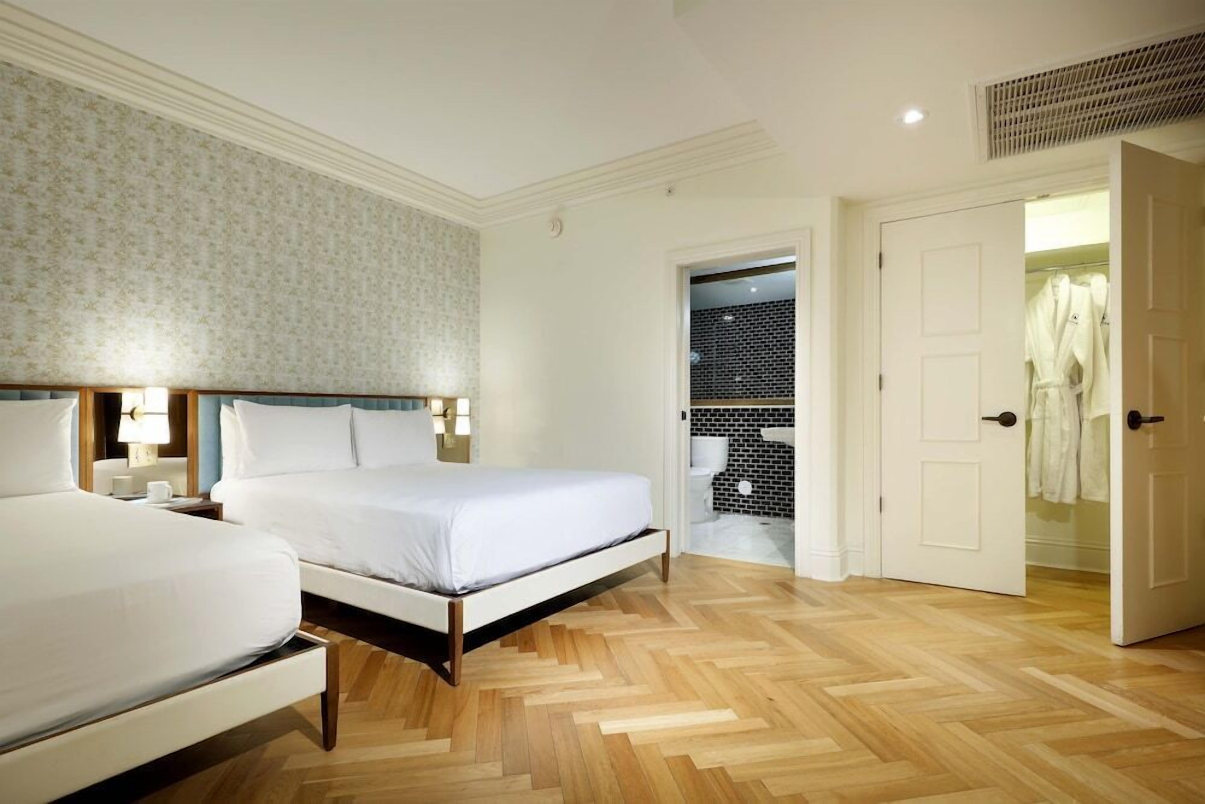 Una habitación de hotel con una cama, mesitas de noche, un armario y un baño visible a través de una puerta abierta.