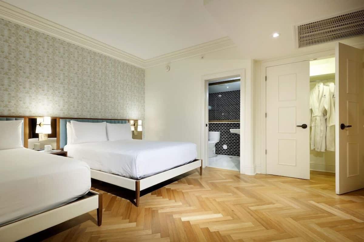 A hotel room with a bed, bedside tables, a wardrobe, and a bathroom visible through an open door.