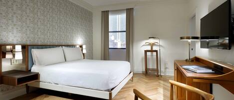Habitación de hotel con cama, mesitas de noche, escritorio, silla, televisor y ventana con cortinas.
