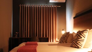 A hotel room with a bed, pillows, a nightstand, a lamp, and a curtain. - The Lot Boutique (Lima)