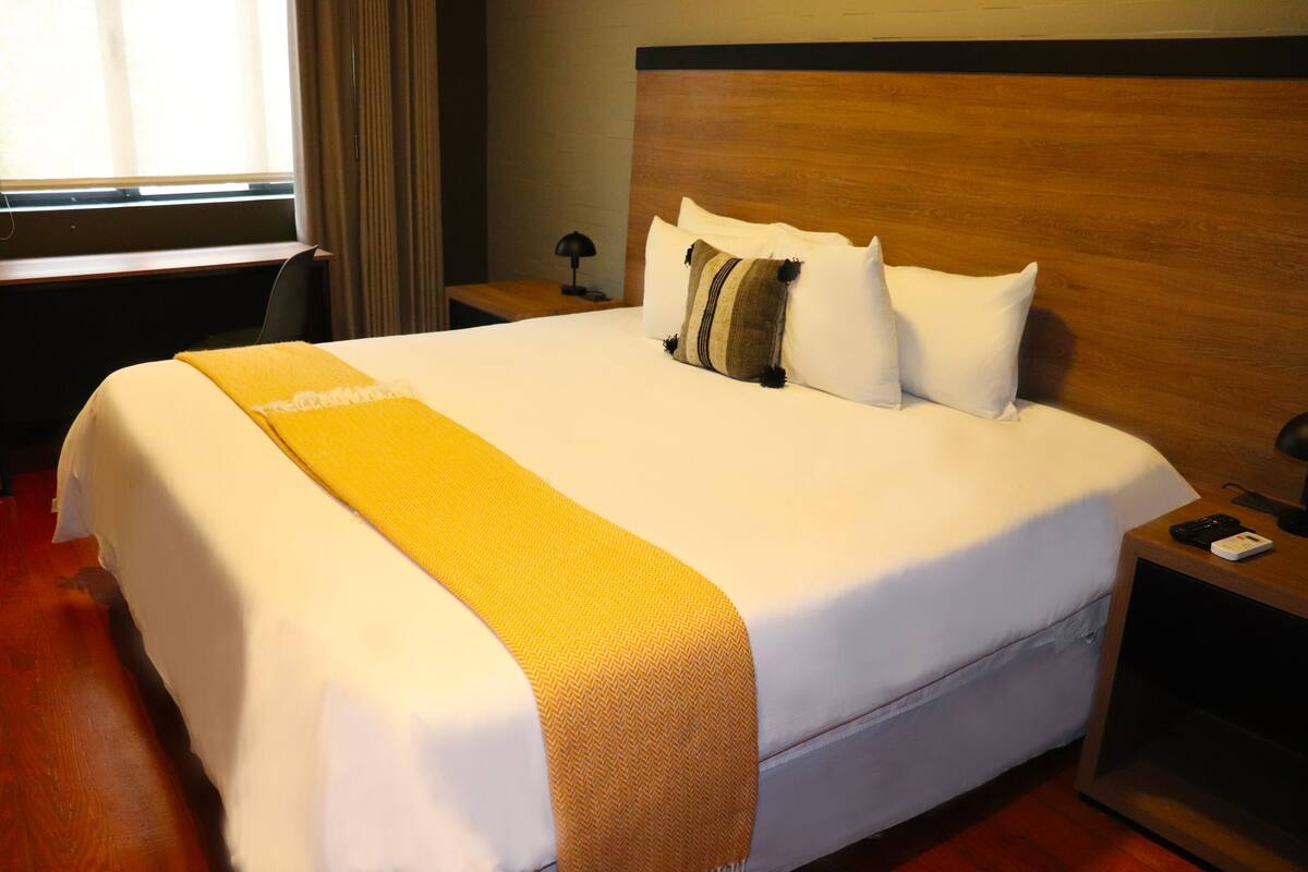 A neatly made bed with a white and yellow bedspread, a wooden headboard, and a nightstand with a lamp.
