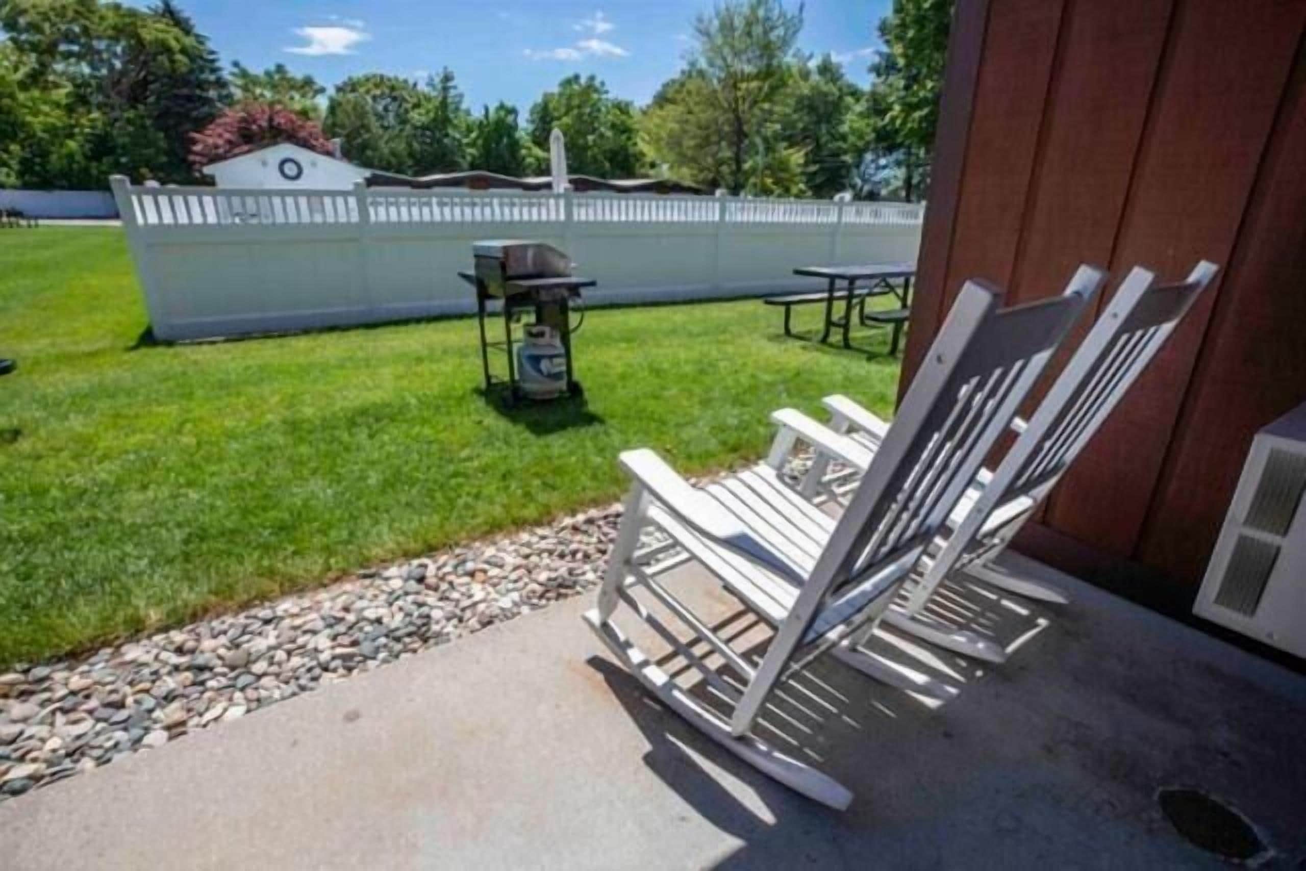 A patio area with a concrete floor, a grill, and white folding chairs.