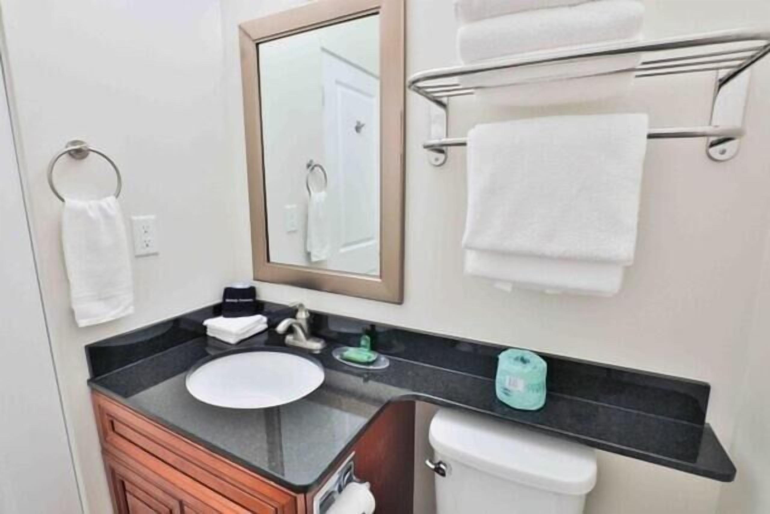 Un baño con lavamanos, espejo, toallero y retrete.