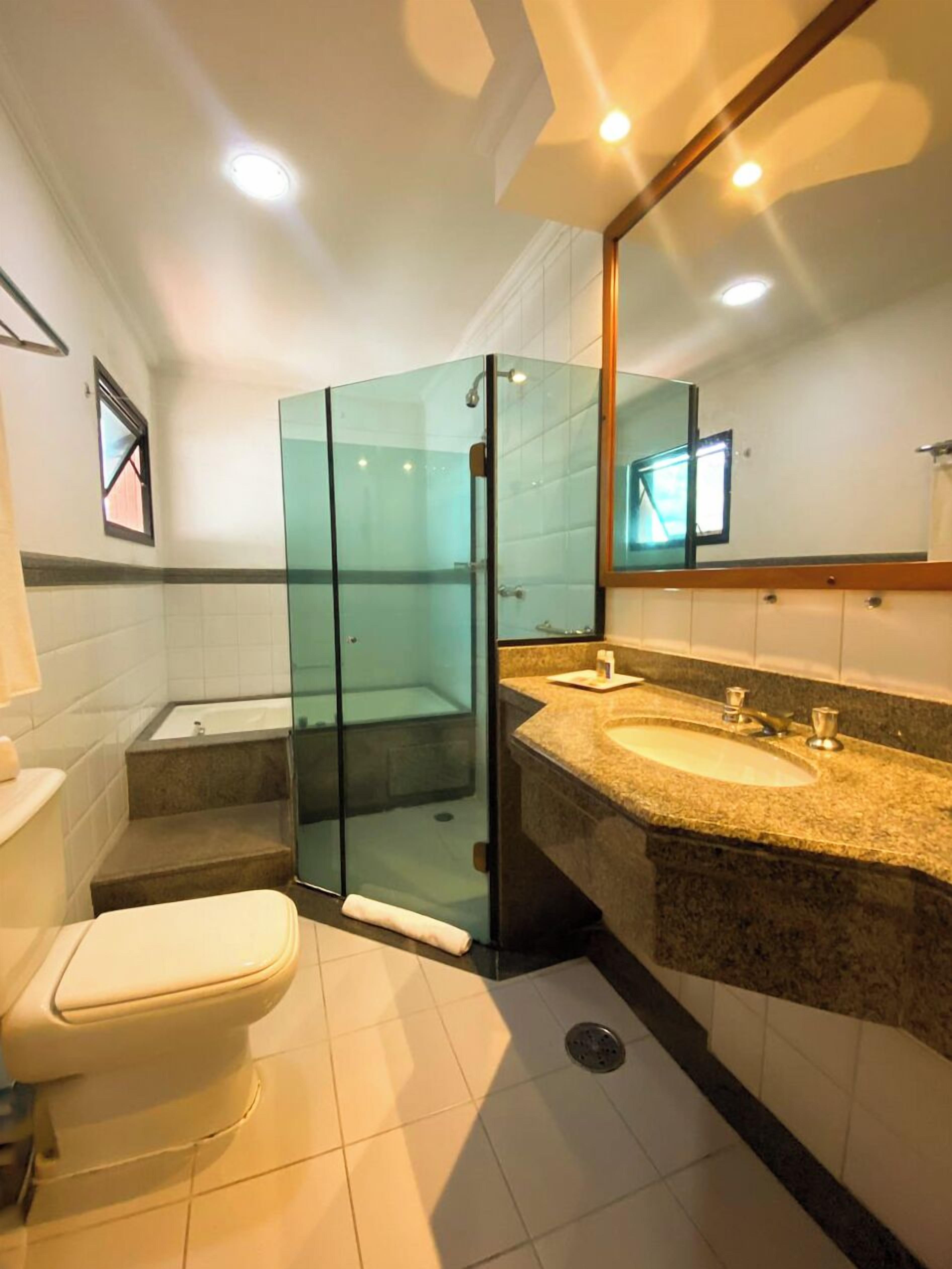 A modern bathroom with a glass shower enclosure, a bathtub, and a granite countertop sink.