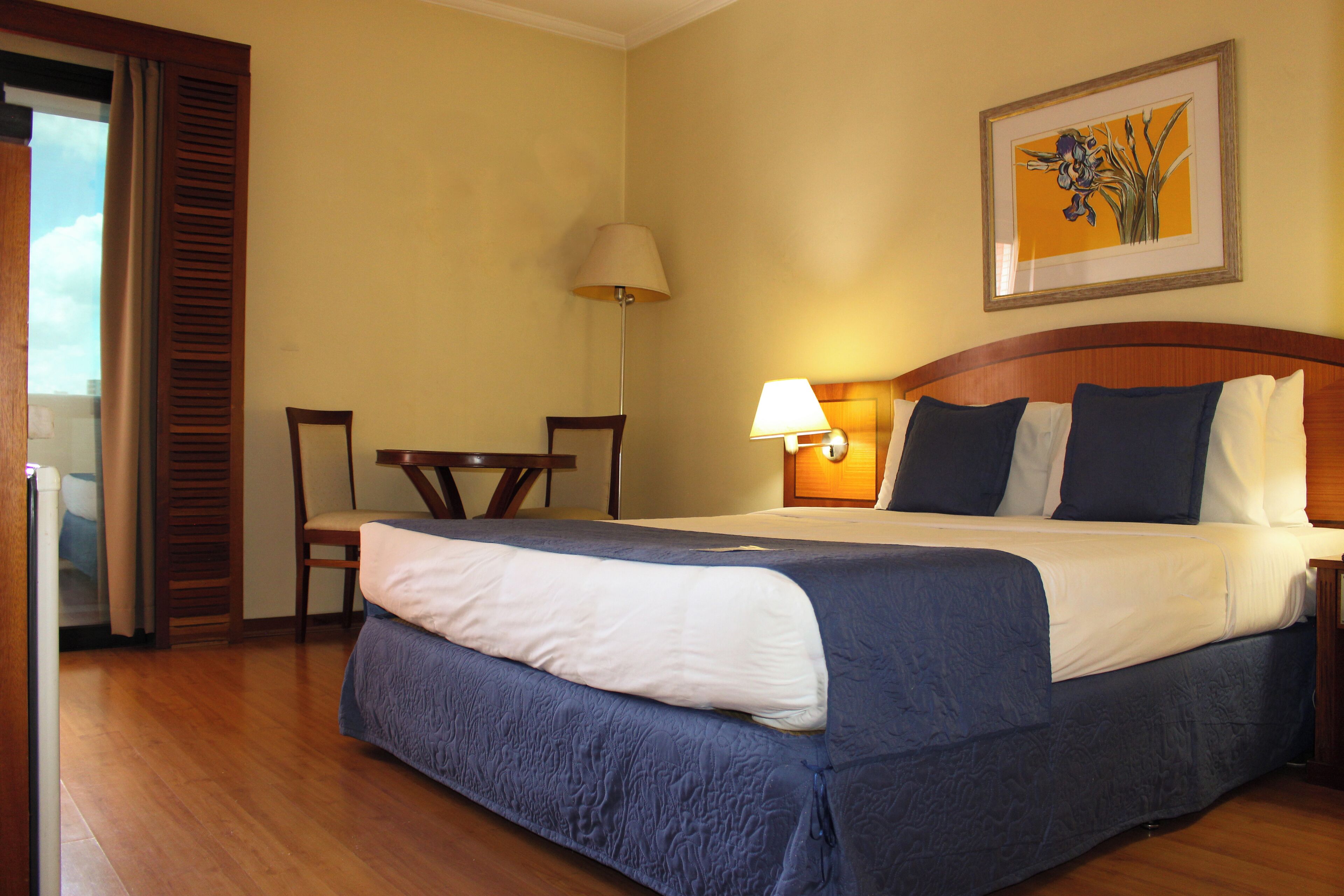 Una habitación de hotel con una cama grande, un escritorio, una silla y una lámpara.
