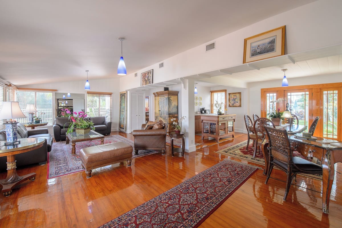 A spacious living room with a wooden floor, a dining area with a wooden table and chairs, and a kitchen area with a wooden cabinet.
