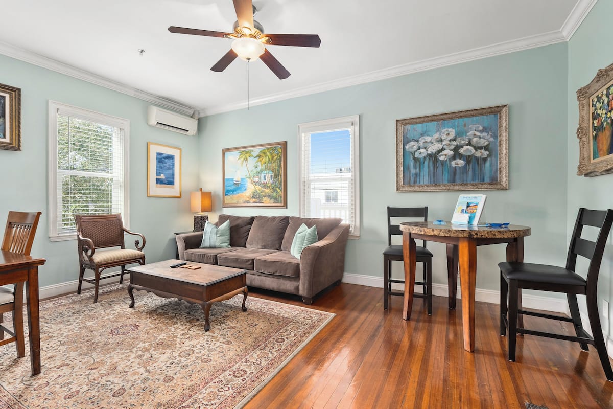 A living room with a wooden floor, a ceiling fan, a sofa, a coffee table, and a rug.