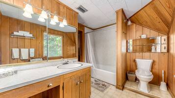 A wooden bathroom with a large mirror, vanity, bathtub, and toilet.