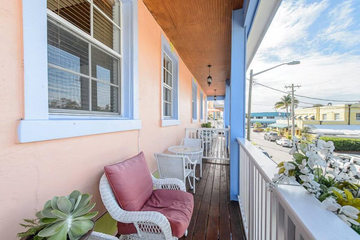 A covered porch with wicker furniture, a pink cushion, and a view of the street.