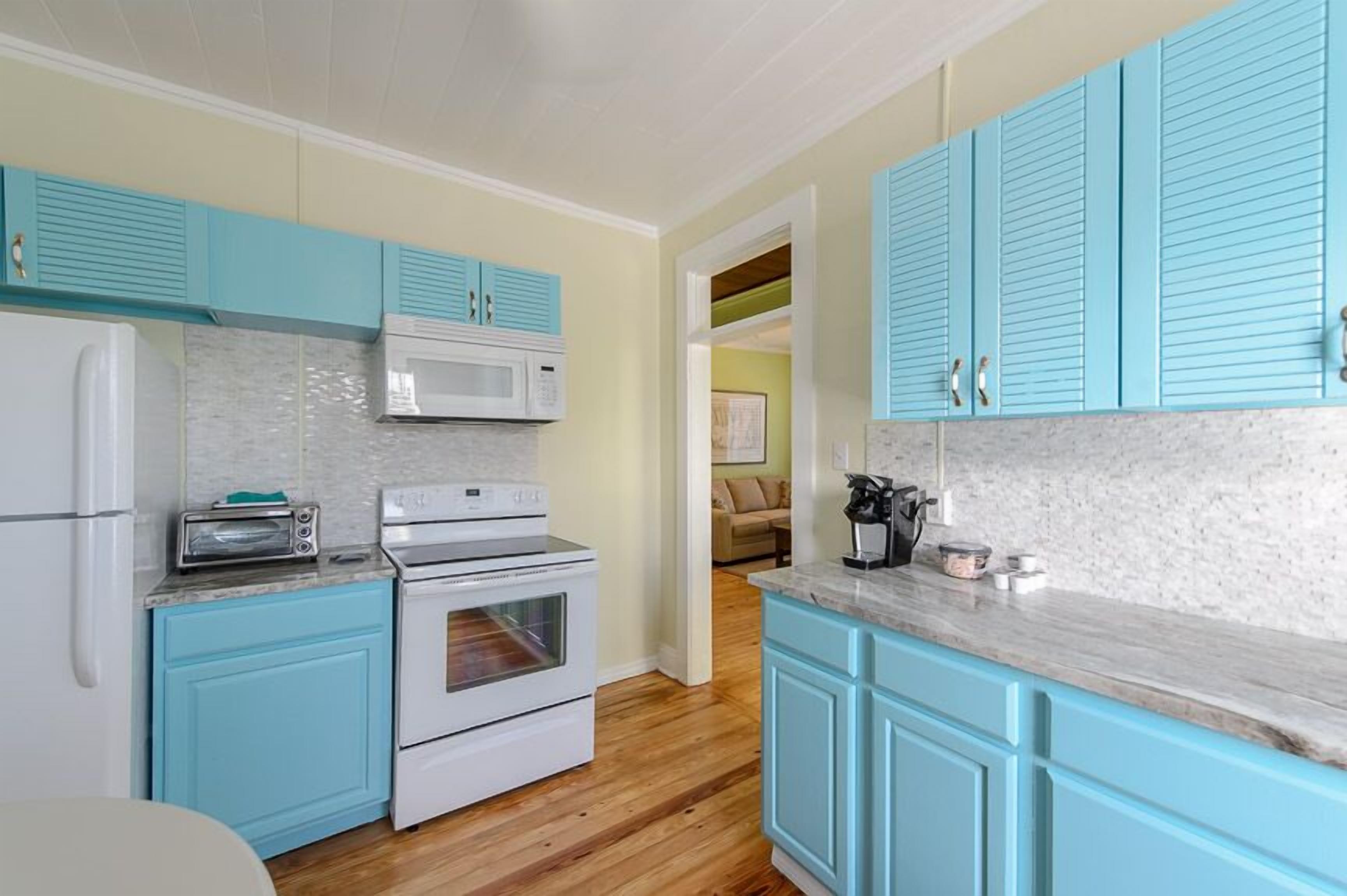 Une cuisine avec des meubles de couleur turquoise, un réfrigérateur blanc, un four à micro-ondes, un grille-pain et un four traditionnel.